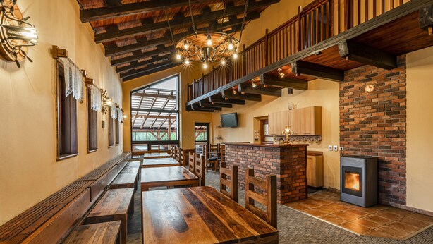 A spacious dining area with wooden benches and tables, a brick fireplace, and a modern kitchen area with a TV. - Chata Ještědka (Svetla pod Jestedem)