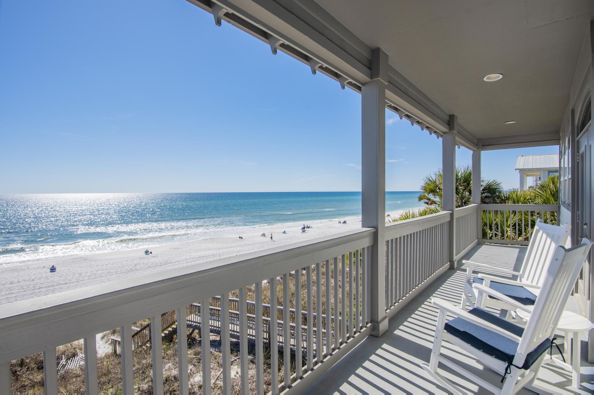 A beach view from a covered porch with white railings and benches.
