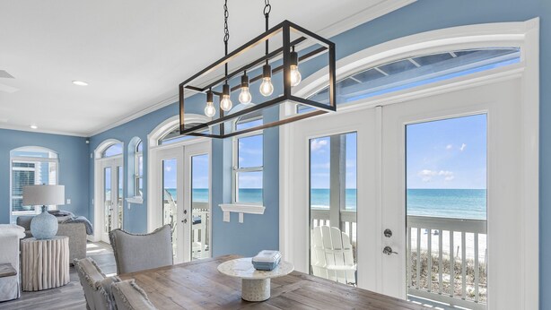 A spacious room with a wooden dining table, a hanging light fixture, and large windows offering a view of the ocean. - Beachfront with Bikes, In-House Gym and LSV (Santa Rosa Beach)