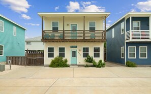 A two-story residential building with a front porch, a balcony, and a small front yard. - Near Beach, Pool & Pet Friendly - Lemon Chill (Port Aransas)