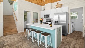A modern kitchen with a central island, bar stools, a stainless steel refrigerator, and a wooden ceiling. - Lemon Chill Home, Arcade, Pool & Near Beach (Port Aransas)