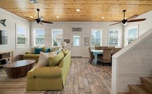 A spacious living room with a wooden ceiling, a sofa set, a dining table with chairs, and a staircase. - Lemon Chill Home, Arcade, Pool & Near Beach (Port Aransas)