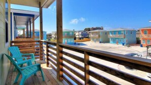 A wooden deck with chairs, a view of colorful buildings, and a clear blue sky. - Lemon Chill Home, Arcade, Pool & Near Beach (Port Aransas)