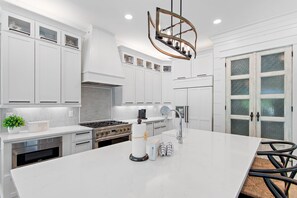 A modern kitchen with white cabinetry, a central island, stainless steel appliances, and a decorative chandelier.