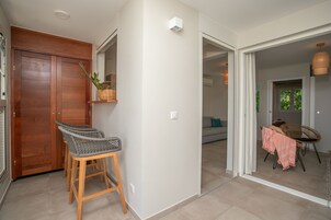 Un pasillo con una puerta de madera, una silla de mimbre y una mesa con mantel rosa.