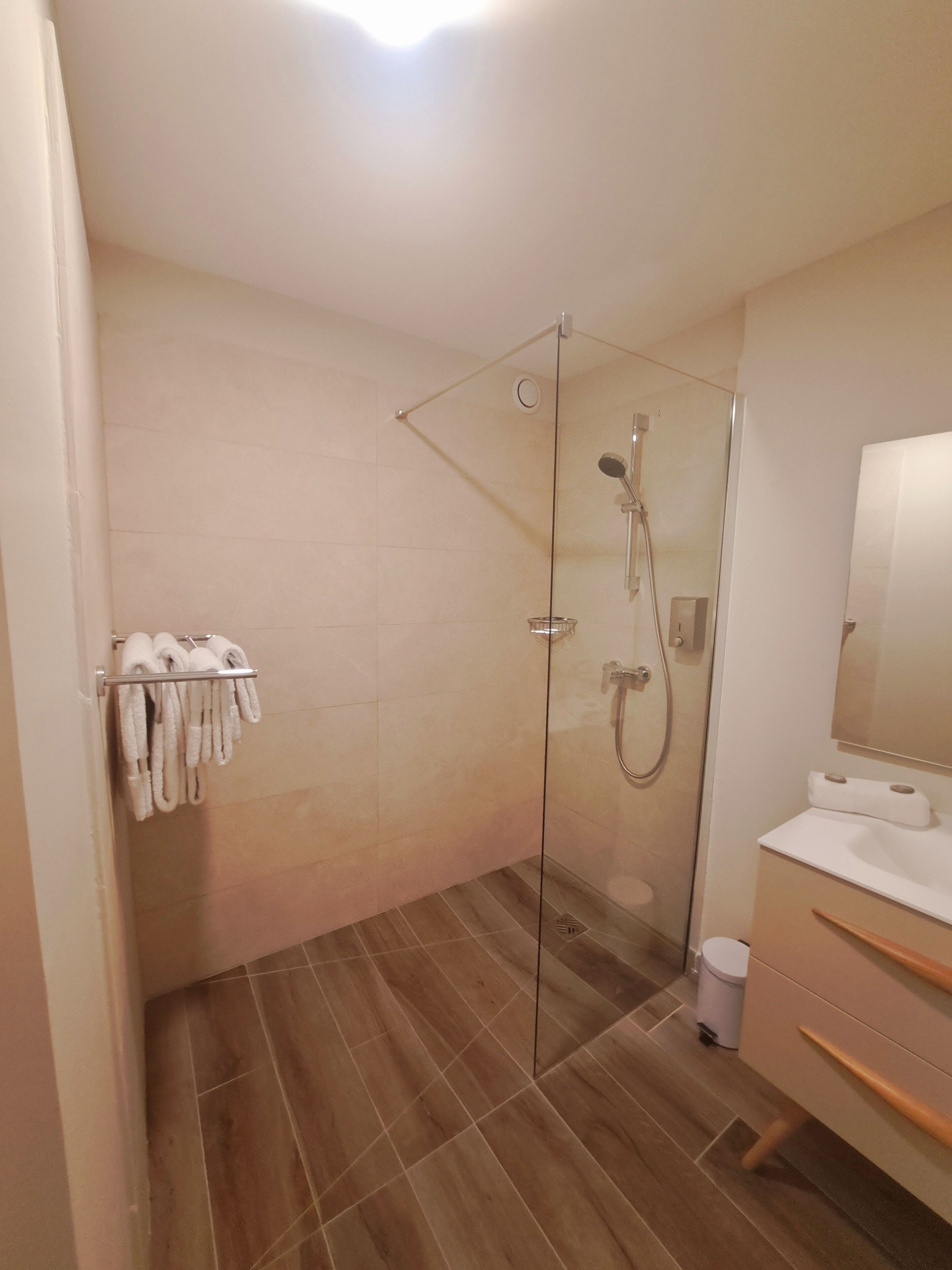 A modern bathroom with a glass-enclosed shower, a white sink, and a towel rack with multiple towels.