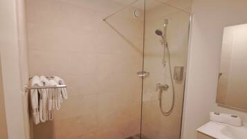 A modern bathroom with a glass-enclosed shower, a white sink, and a towel rack with multiple towels.