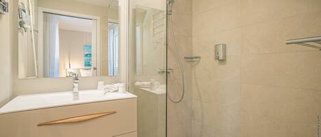 A modern bathroom with a glass-enclosed shower, a white vanity with wooden handles, and a large mirror.