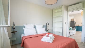 Habitación de hotel con una cama, una mesita de noche, una lámpara fijada a la pared y vistas al área de la cocina contigua.