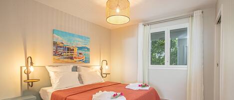 A bedroom with a bed, a painting, a window, and a hanging light fixture.