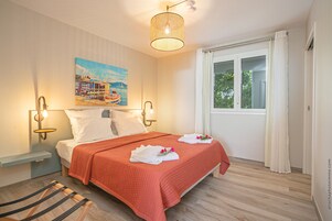 Un dormitorio con cama, un cuadro, una ventana y una lámpara colgante.