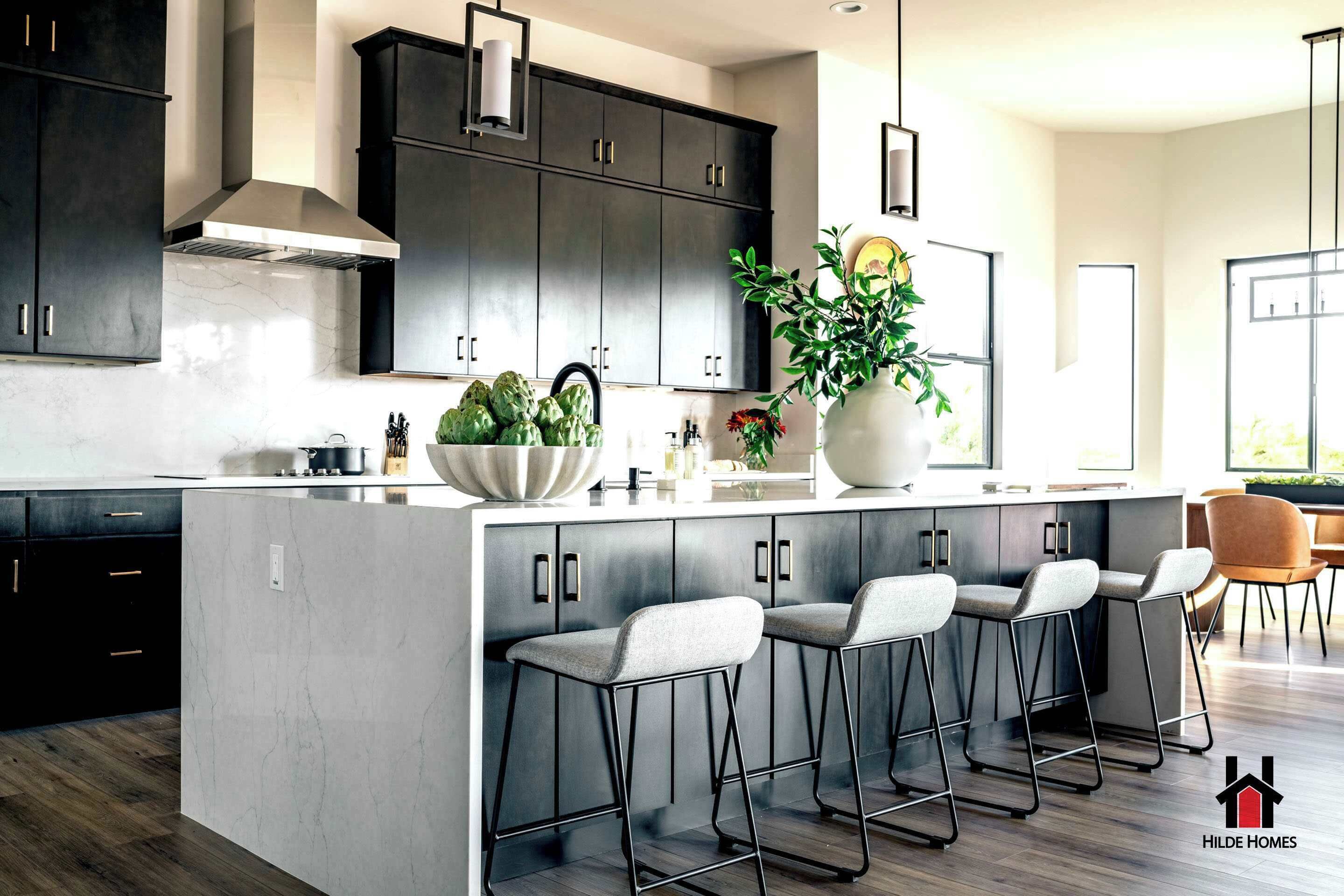 A modern kitchen with dark cabinets, a marble countertop, and a central island with bar stools.