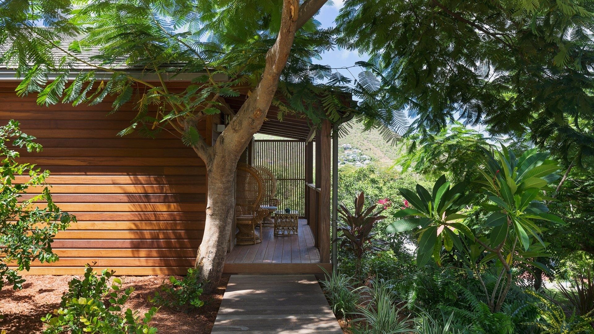 Ein hölzernes Gebäude mit überdachter Veranda, umgeben von üppiger Vegetation und Blick auf die Landschaft.