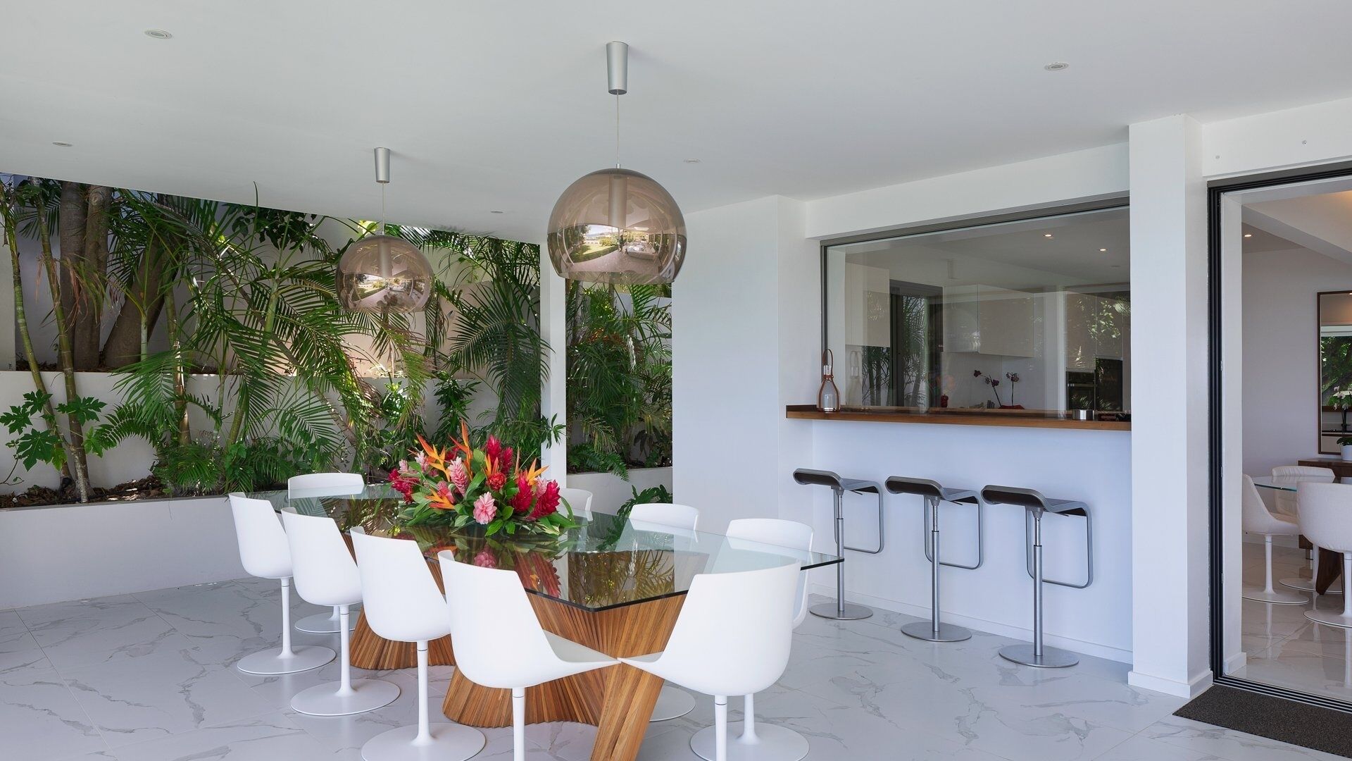 Un espace repas moderne avec une table en verre, des chaises blanches et un arrangement floral central.