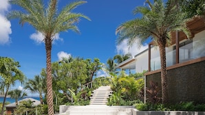 A modern building with a staircase leading to a glass balcony, surrounded by palm trees and lush greenery. - Stellae (1/6 Rooms) Luxury villa (Anse de Lorient)