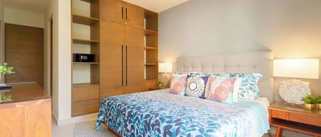 Une chambre à coucher avec un grand lit, une armoire à plusieurs compartiments, une table de chevet avec une lampe et une petite plante.
