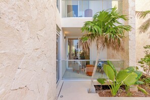 A modern building with a glass balcony, a palm tree, and a small garden area. - Ocean-View Patio, 9 Pools & Beach Club (Akumal)
