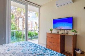 A bedroom with a bed, a TV, a wooden dresser, and a view of the outdoors.