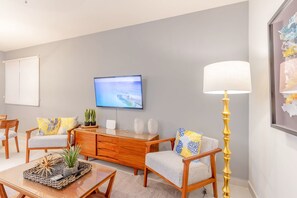 A modern living room with a flat-screen TV mounted on the wall, a wooden coffee table, two armchairs, a sofa, and a floor lamp. - Ocean-View Patio, 9 Pools & Beach Club (Akumal)