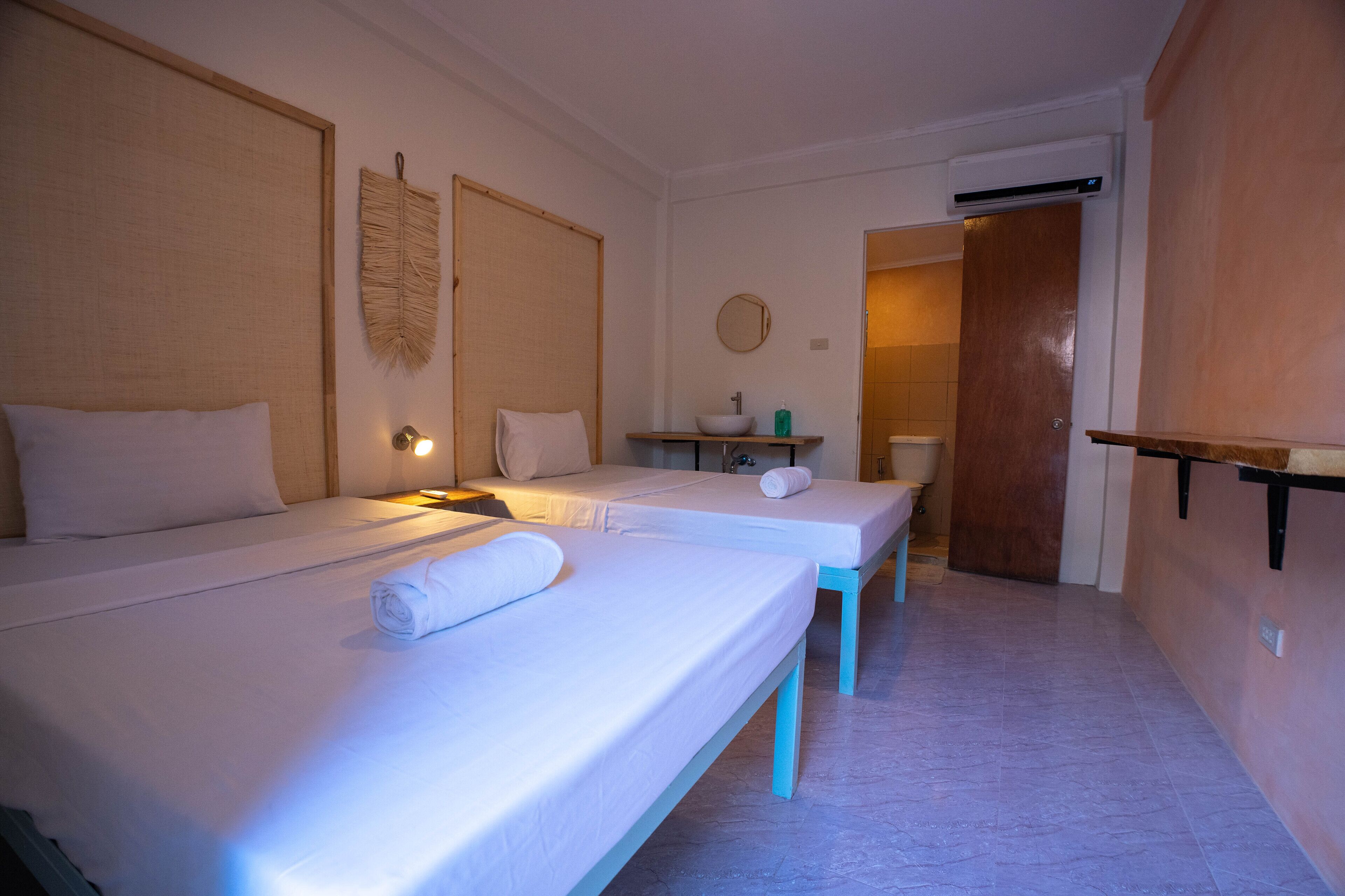 Ein Hotelzimmer mit zwei Betten, einem kleinen Badezimmer und einer Holztür.