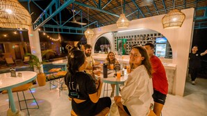 A group of people seated at a round table in a modern indoor setting with exposed beams and pendant lighting. - Mad Monkey Panglao (Dauis)