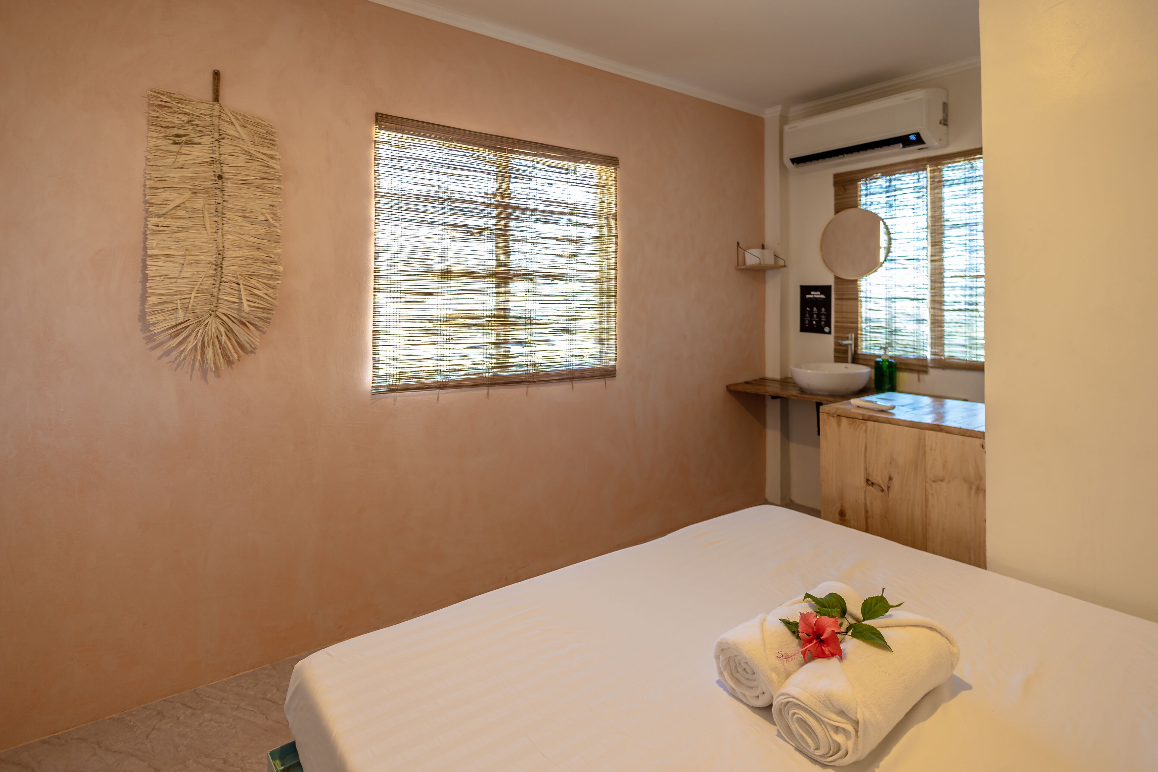 A bedroom with a bed, a window with blinds, a wall-mounted air conditioner, and a wooden cabinet with a sink.