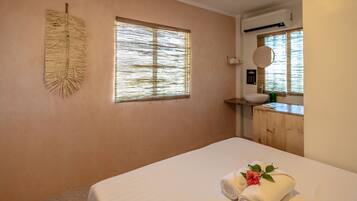 A bedroom with a bed, a window with blinds, a wall-mounted air conditioner, and a wooden cabinet with a sink.
