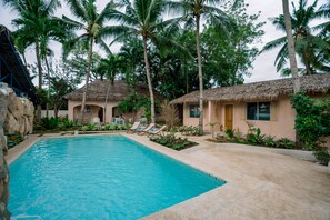 A swimming pool surrounded by thatched-roof cottages, palm trees, and a stone wall. - Mad Monkey Panglao (Dauis)