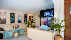 A reception area with a wooden reception desk, a laptop, a fan, and a large vase with flowers. - Mad Monkey Panglao (Dauis)