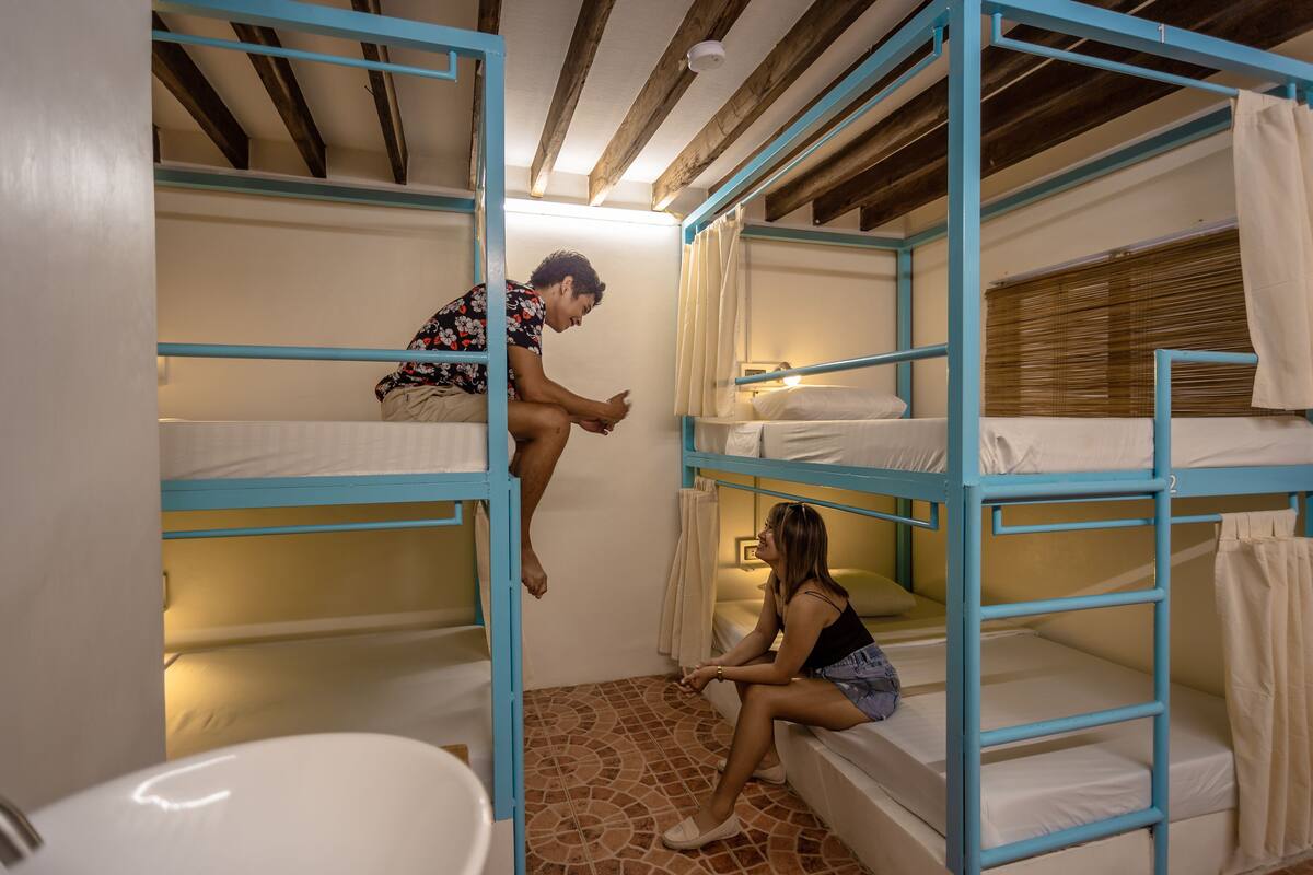 Une chambre avec un lit superposé, un carrelage au sol, un lavabo et une fenêtre avec des stores.