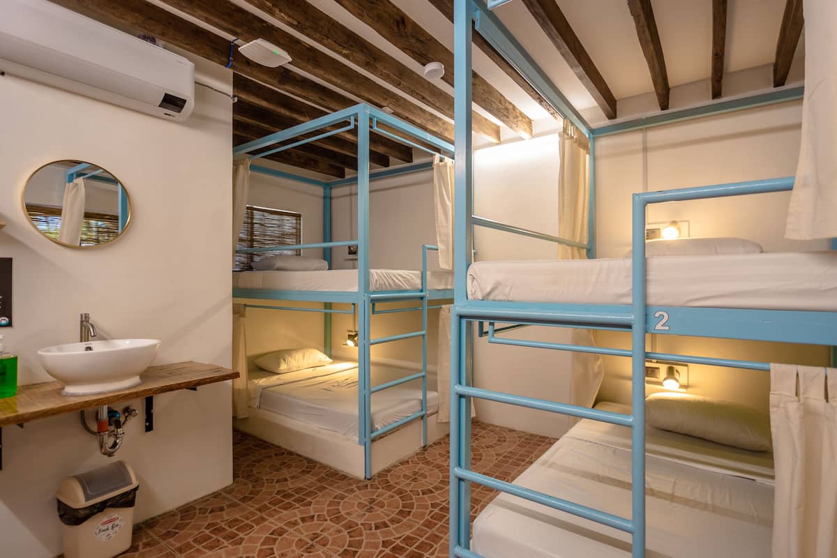 Une chambre avec des lits superposés, un lavabo, un miroir et une poubelle.