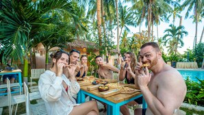 A group of people dining outdoors at a table with a pool in the background. - Mad Monkey Panglao (Dauis)