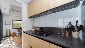 Ett modernt kök med en gasspis, en brödrost och en kaffebryggare. Det finns ett fönster med persienner och en dörr som leder till ett annat rum.
