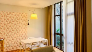 A modern living room with a white table, a sofa, and a large window with curtains.