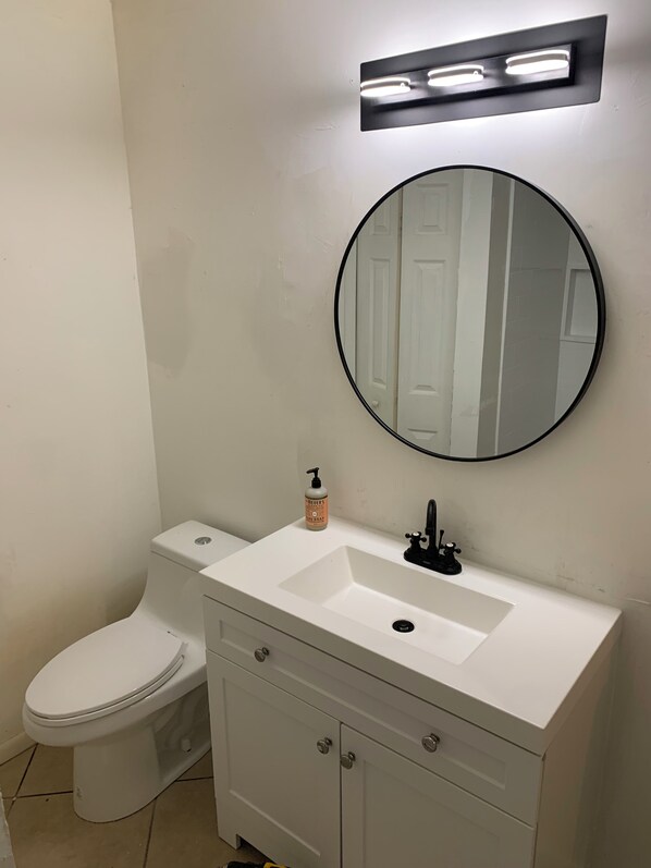 A bathroom with a white sink, a round mirror, a toilet, and a soap dispenser.
