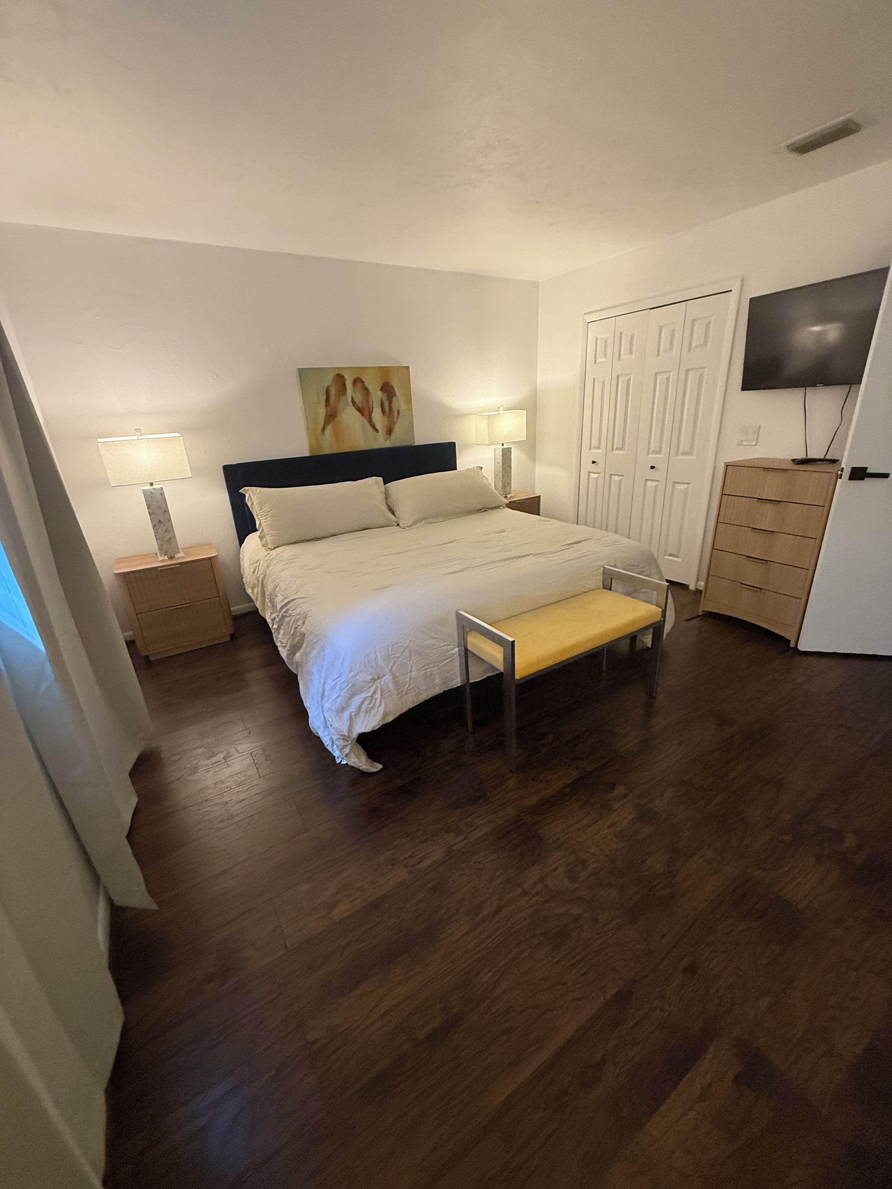 A bedroom with a bed, bedside tables, a bench, a wardrobe, and a television.