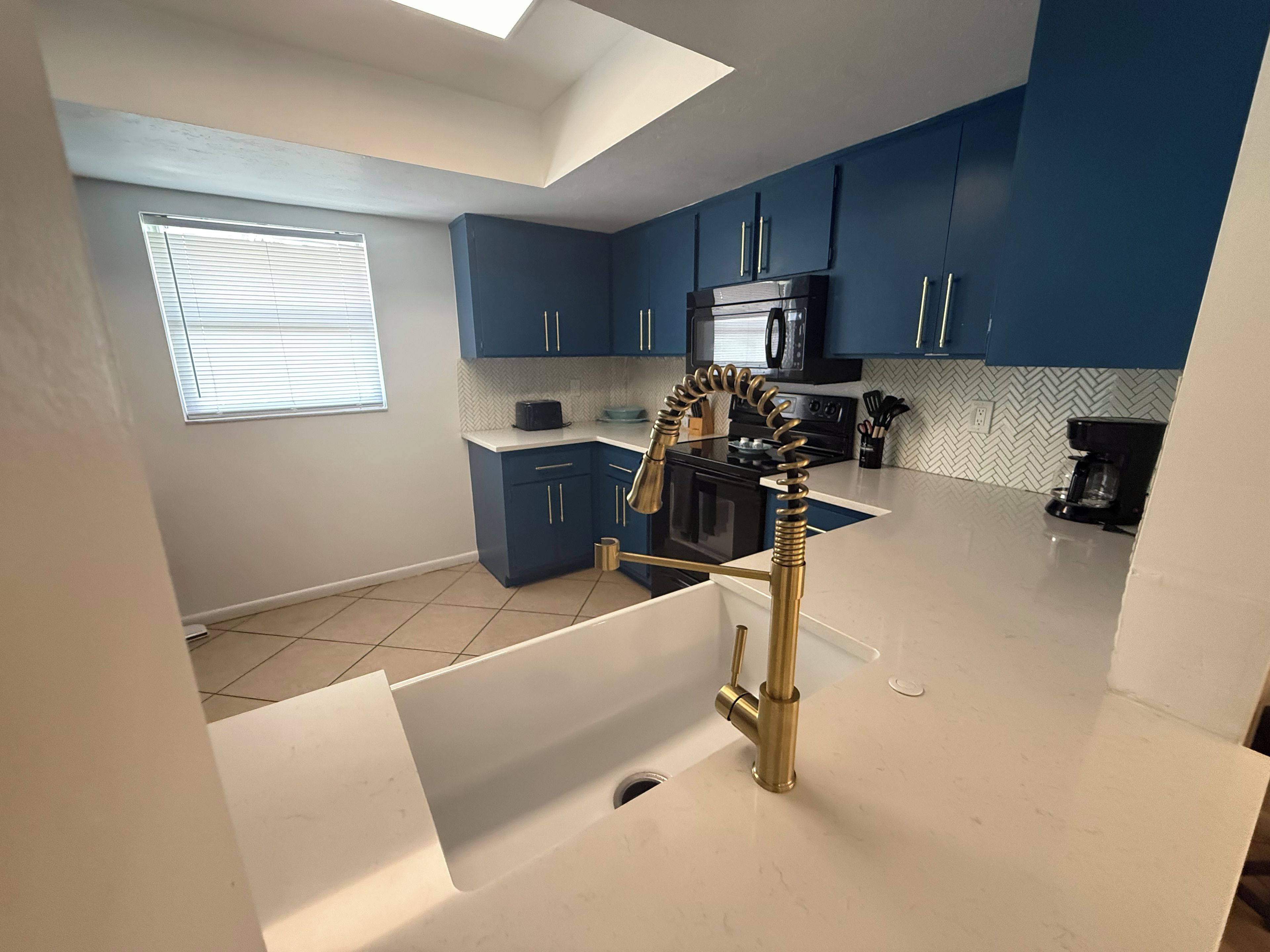A modern kitchen with blue cabinets, a black microwave, and a unique gold faucet.