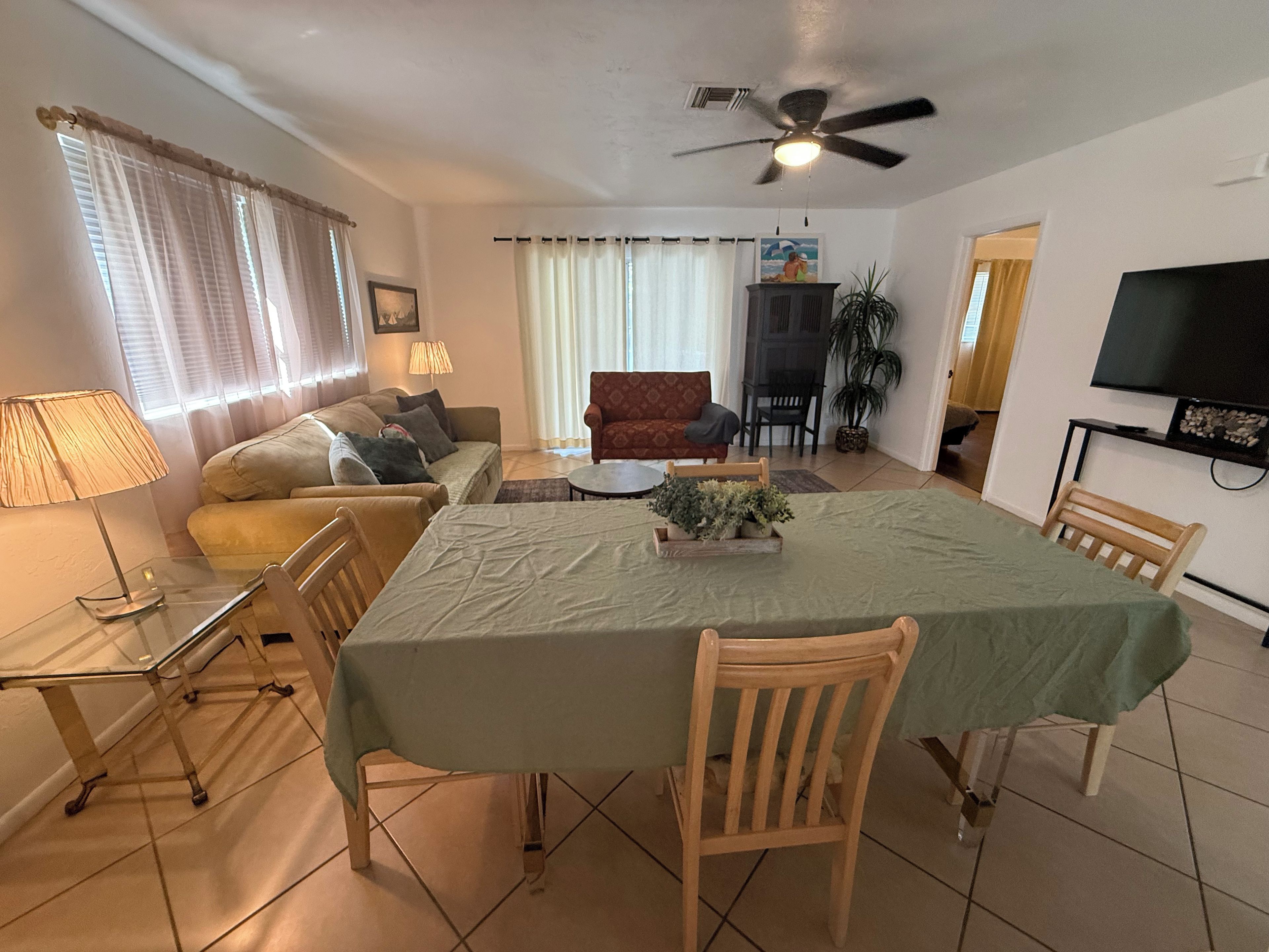 A living room with a dining table, sofas, a TV, and a ceiling fan.