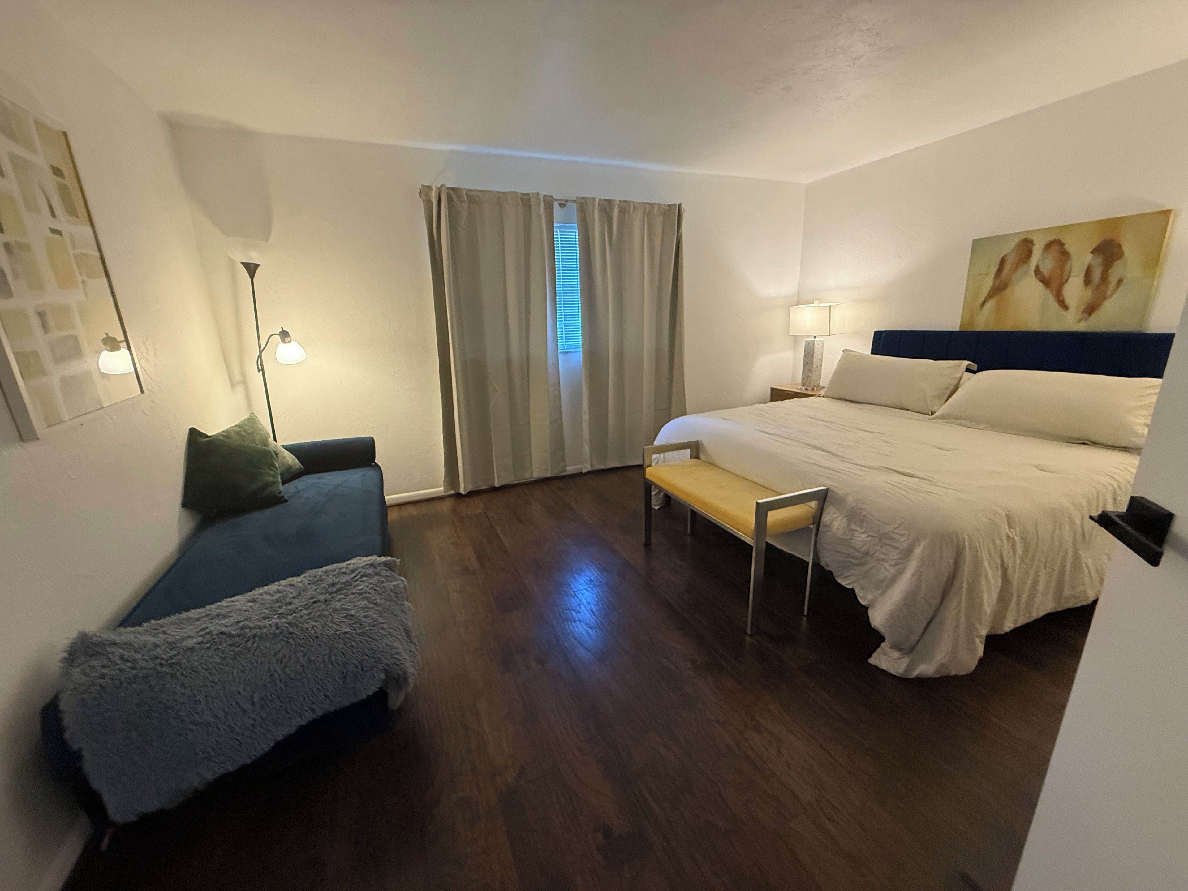 A hotel room with a bed, a bench, a sofa, a lamp, and a painting on the wall.