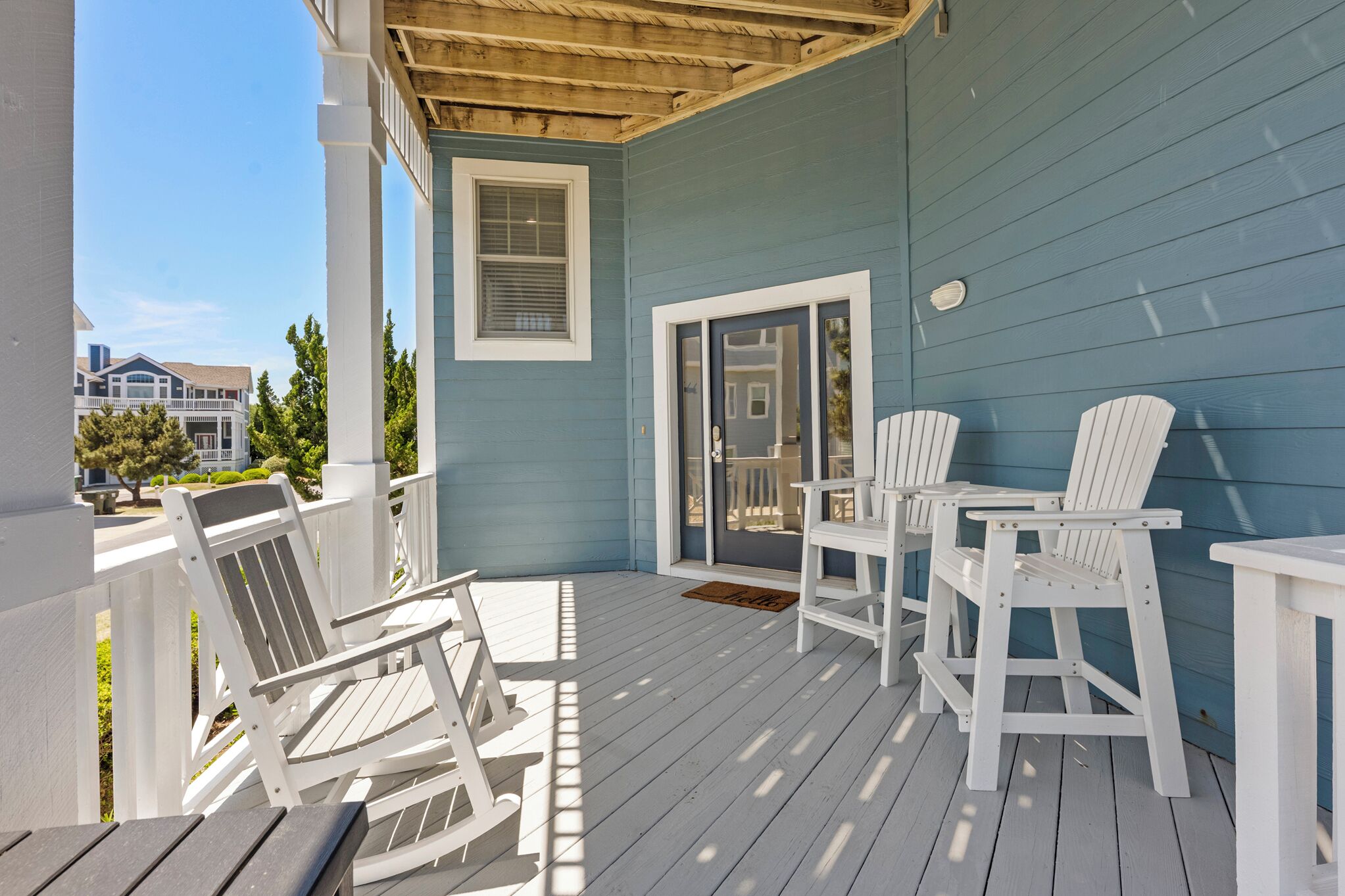 A covered porch with white Adirondack chairs, a small table, and a sliding glass door leading to an interior space.