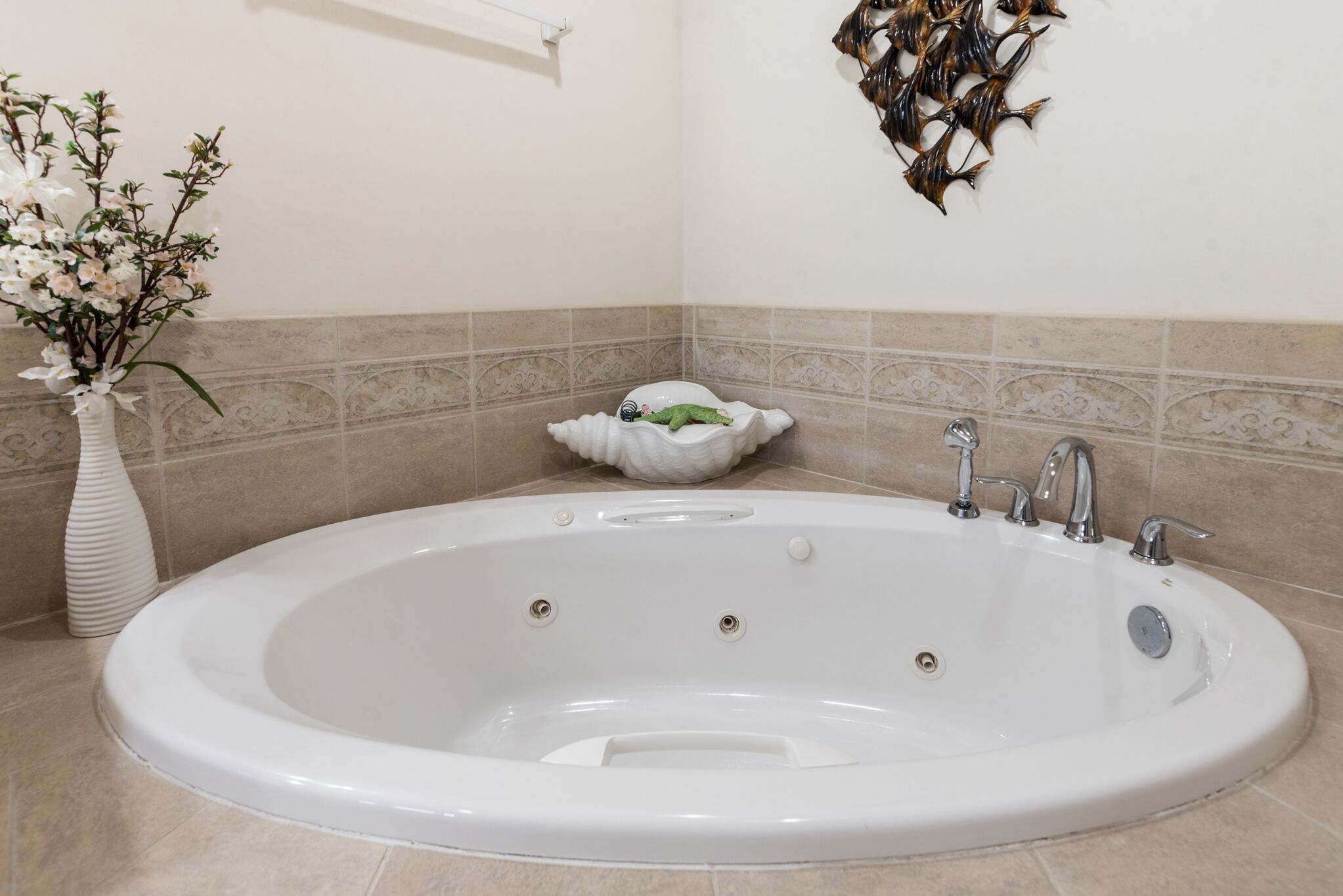 A bathroom with a large oval bathtub, a white vase with flowers, and a wall-mounted fish decoration.