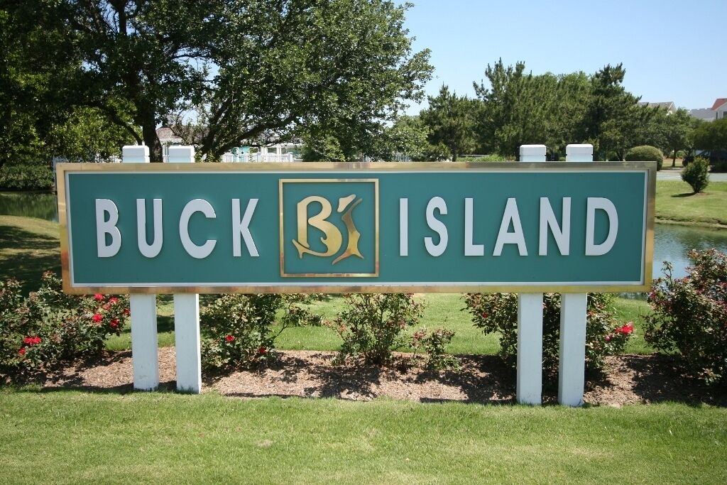 Un letrero de Buck Island con un logotipo, rodeado de vegetación y un estanque.