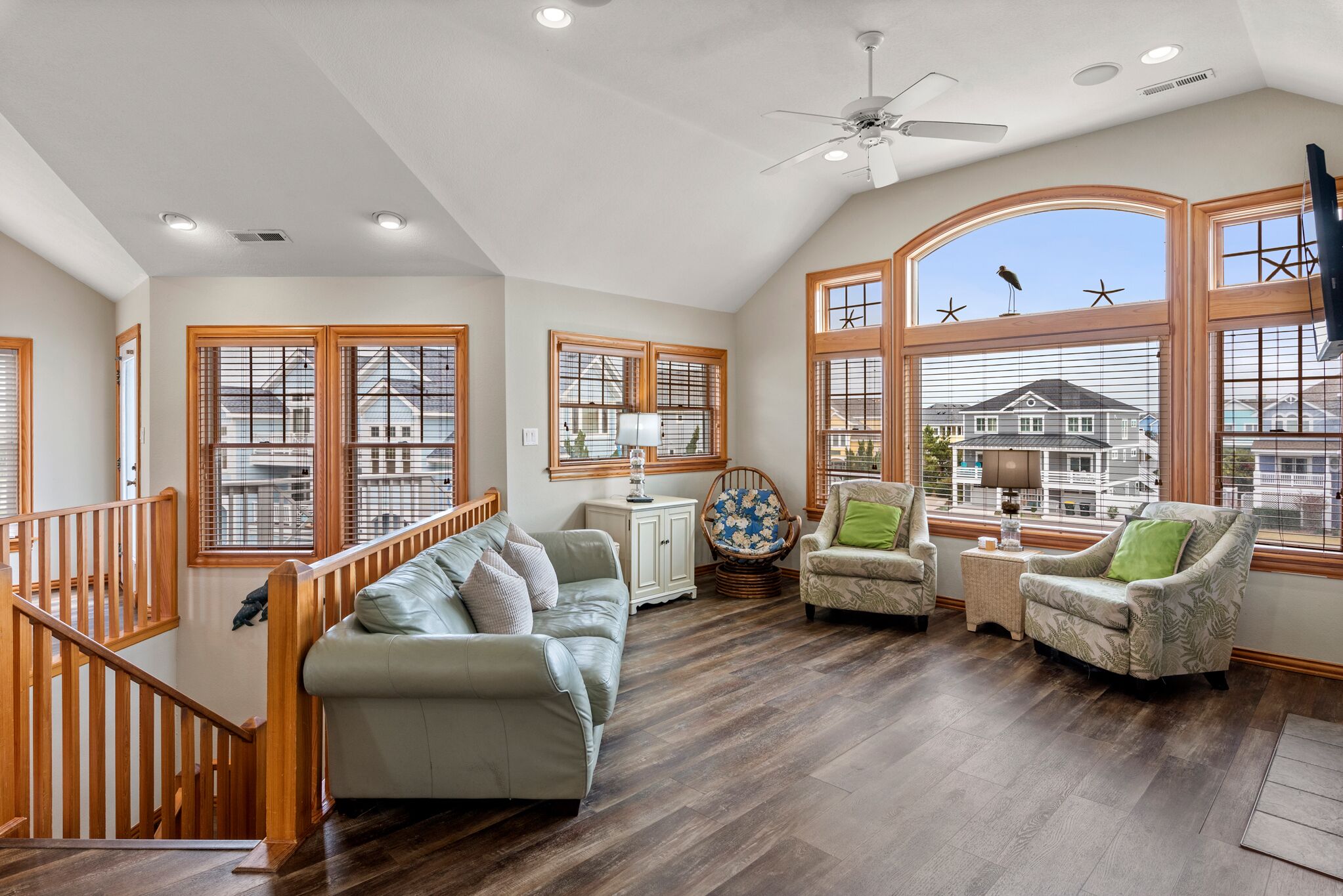 A spacious living room with a high ceiling, large windows, and a staircase.