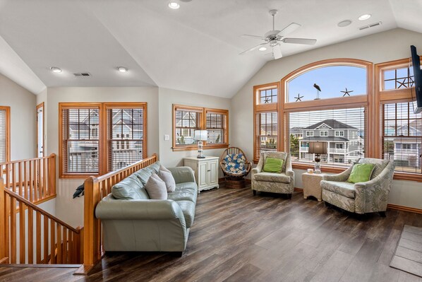 Un salon spacieux avec un plafond haut, un plancher en bois et de grandes fenêtres décorées de motifs d’étoiles de mer.