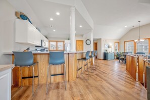 A spacious kitchen with wooden flooring, white cabinets, and a bar area with stools. - White Dolphin: Hot Tub | Pool Access | Dogs OK (Corolla)