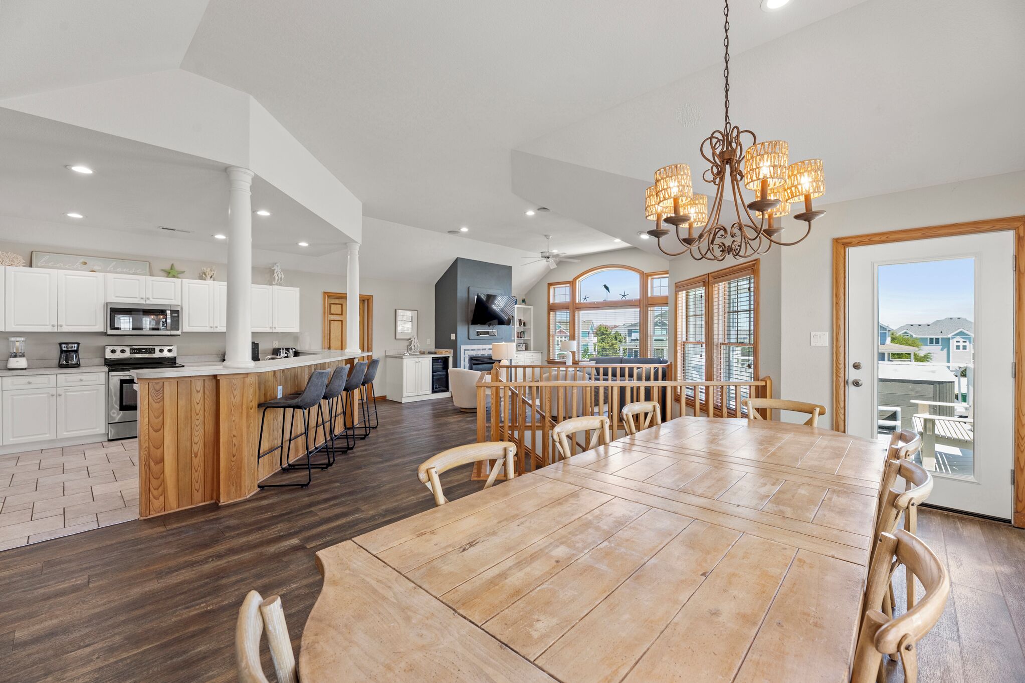 A spacious kitchen with a central island, a dining area with a large wooden table, and a view of the outdoors through large windows.