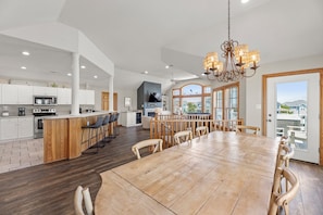 A spacious kitchen with a central island, a dining area with a large wooden table, and a view of the outdoors through large windows.