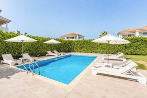 Ein Pool mit Liegestühlen und Sonnenschirmen, umgeben von einer Hecke und Gebäuden.