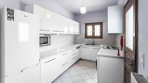 Een kleine keuken met witte kastjes, een magnetron, een fornuis en een raam met zonwering.