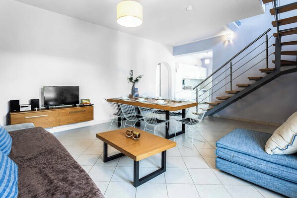 Una sala moderna con sofá, mesa de centro, televisor y comedor.